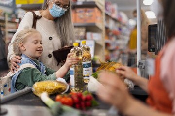 Grandmother with her little granddaughter shopping in supermarket, putting products on checking desk