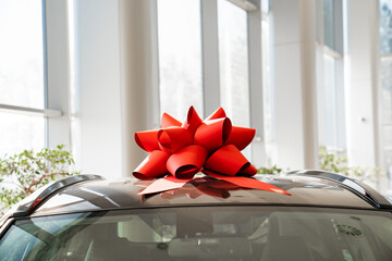 a red gift bow on the roof of a new car in the car dealership. 