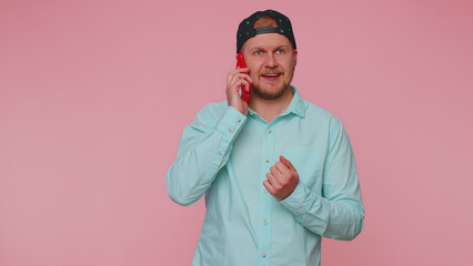Man 30s in blue shirt having pleasant mobile conversation using smartphone with friends, telling good news. Young adult blonde guy talking on cell phone isolated alone on pink studio wall background