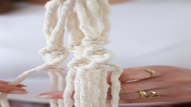Close up of freelancer woman working on half-finished macrame piece, weaves flower pot holder. Women hobby.