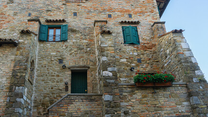Fototapeta na wymiar Traditional brick-style building in Italy, with green shutters and flowers.