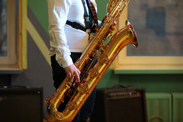A large golden baritone saxophone in close-up in the hands of a standing musician inside the room...