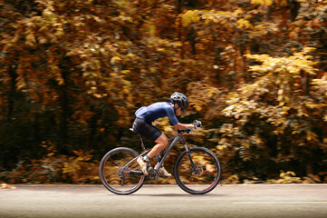 Fototapeta na wymiar Cycling training, Cyclist speeding mountain bike on road with autumn forest side. Outdoor sport activity fun and enjoy riding. Basic techniques training on trail of athletes. Focusing on cyclist