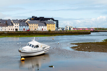 Obraz premium Small boat at low tide. River Corrib, Claddagh area in the background. Galway city Ireland. Popular town landmark and tourist attraction. Blue cloudy sky.