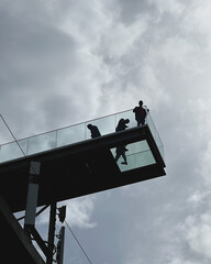 Menschen auf einem Skywalk vor grauem Himmel 