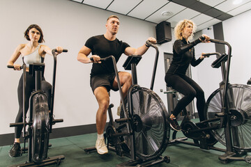 Young man and women using air bike for cardio workout at cross training gym
