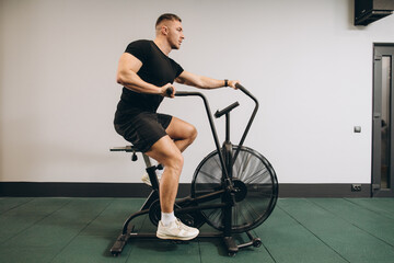 Fototapeta na wymiar Strong man using air bike for cardio workout at cross training gym.