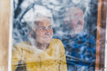 loving senior European couple looking through the window at home medium closeup indoor seniority concept. High quality photo