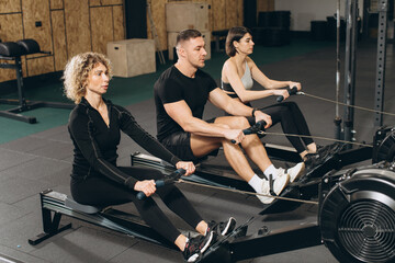 Fototapeta na wymiar Young man and beautiful women working out with rowing machine at crossfit gym.
