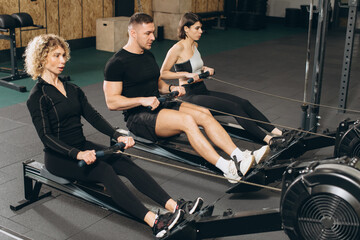 Young man and beautiful women working out with rowing machine at crossfit gym.