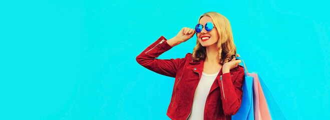 Obraz na płótnie Canvas Colorful portrait of stylish happy smiling young woman with shopping bags posing wearing red jacket on blue background