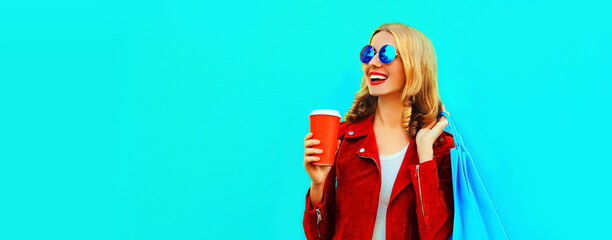 Colorful portrait of stylish happy smiling young woman with shopping bags posing wearing red jacket on blue background