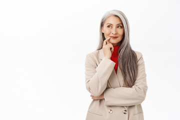 Portrait of korean businesswoman, woman with grey hair thinking, wearing suit, smiling intrigued,...