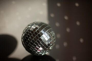 Disco ball reflects light in room. Ball of small mirrors stands on surface of speaker.