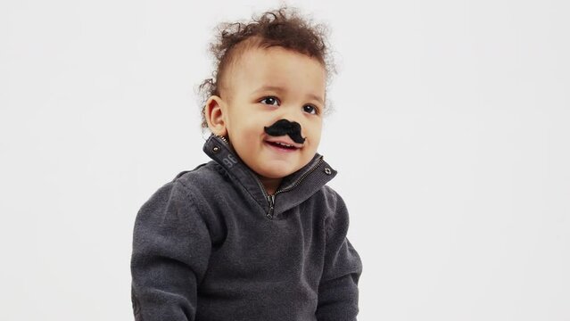 Afro American curly-haired boy sticks fake moustache to his face medium closeup copy space movember grey background studio shot . High quality 4k footage