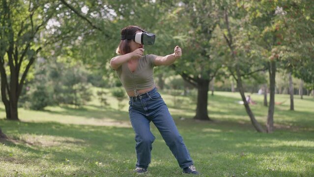 Excited happy young woman with dwarfism in VR headset laughing out loud gaming in park forest outdoors. Wide shot carefree Caucasian little person enjoying leisure playing video games