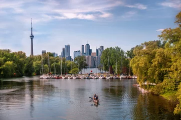 Foto auf Acrylglas Toronto, Ontario, Canada - 06 16 2018: Summertime view of the marina on Toronto Centre Island with rows of yachts, a couple in a boat in foreground and the downtown Toronto skyline in background © Vadim Rodnev