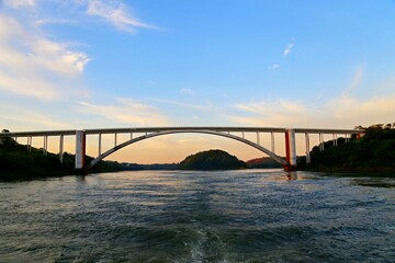 Bridge over the Iguacu River on the border between Brazil and Paraguay. Arch bridge over the waters of the river and an island in the background. Dusk sky.