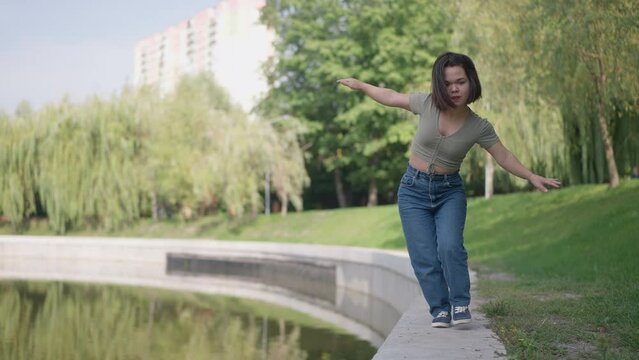 Wide shot joyful little woman walking on lake shore in slow motion having fun in spring summer park. Happy carefree Caucasian young person with dwarfism enjoying leisure on weekend outdoors