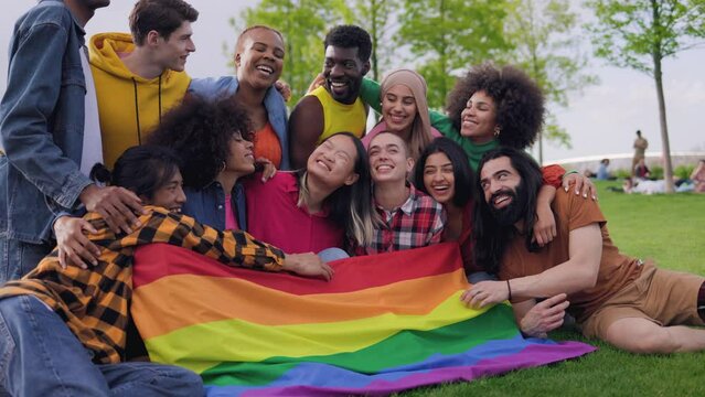 Happy diverse friends holding LGBT rainbow flag having fun together outdoors