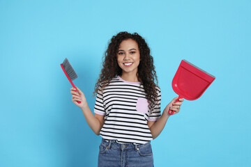 African American woman with broom and dustpan on light blue background