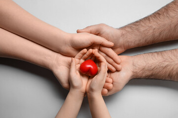 Parents and kid holding red heart in hands on light grey background, top view