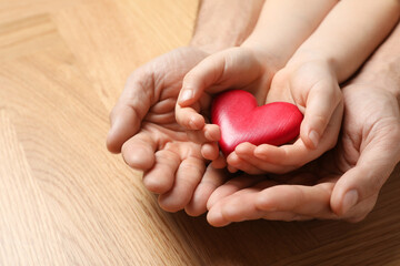 Man and kid holding red heart in hands at wooden table, closeup