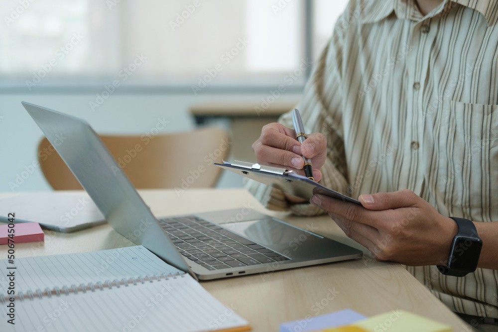 Poster professional businessman using laptop computer and making notes on notepad.