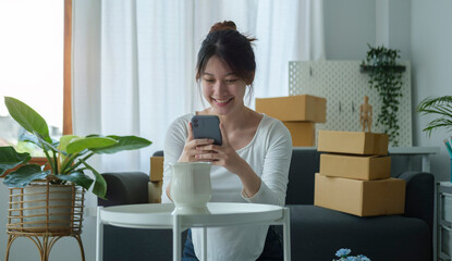 Smiling asian woman online seller using smart phone taking a photo of product for post to sell online on internet.