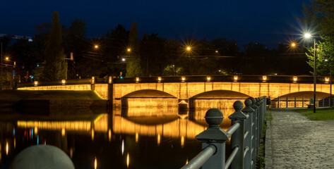 An illuminated stone bridge casting reflections on the calm river surface