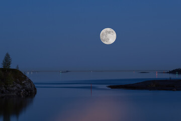 A view from the land towards the sea. Moon casting a reflection on the calm water.