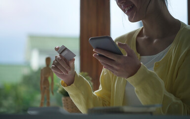 Cheerful young asian woman holding credit card and smart phone for shopping online..