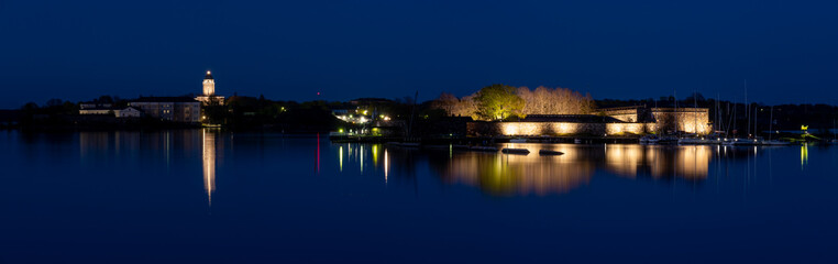 Panoramic view of Suomenlinna island. Illuminated buildings cast reflections on the calm water.