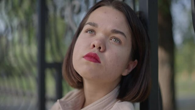 Headshot portrait of sad frustrated young woman with dwarfism sighing looking away sitting in park outdoors. Close-up depressed Caucasian little person thinking procrastinating in slow motion