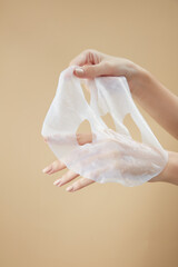 Front view of hand holding a mask in beige background for cosmetic advertising