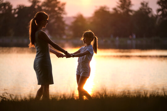 Happy mom and daughter girl relaxing holding hands enjoying time together in summer park at sunset. Family love and relationship concept
