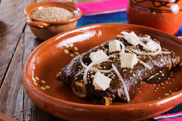 tortillas wrapped in mole poblano with sesame seeds, cheese and onion. enchilas poblanas, mexican food