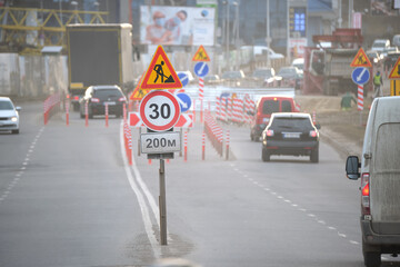 Roadworks warning traffic signs of construction work on city street and slowly moving cars