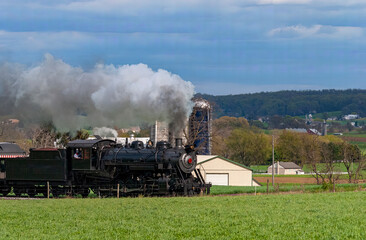 Obraz na płótnie Canvas An Antique Steam Passenger Train Approaching on a Single Track Blowing Smoke on a Cloudy Day