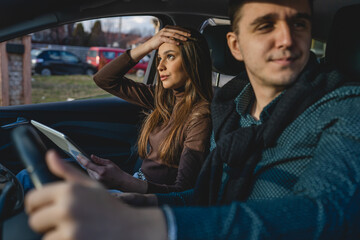 Man and woman young couple or friends male and female boyfriend and girlfriend using digital tablet for navigation searching map for direction arguing while travel in car real people copy space