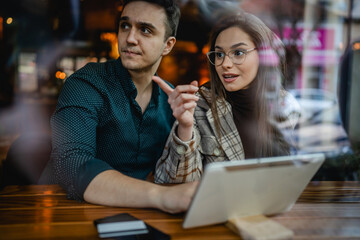 Two people young adult couple woman and man boyfriend and girlfriend or wife and husband sitting at cafe relationship concept woman showing something to the side point finger