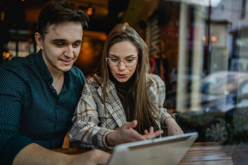 Two people young adult couple woman and man boyfriend and girlfriend or wife and husband sitting at cafe relationship concept use digital tablet for online search or video call real people copy space