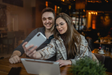 Two people young caucasian couple man and woman female and male friends or boyfriend and girlfriend taking selfie photos or making a video call while sitting at cafe copy space fun and romance