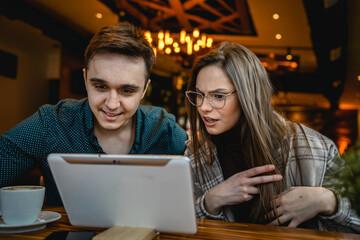 Two people young adult couple woman and man boyfriend and girlfriend or wife and husband sitting at cafe relationship concept use digital tablet for online search or video call real people copy space