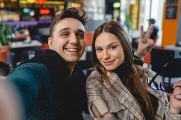 Two people young caucasian couple man and woman female and male friends or boyfriend and girlfriend taking selfie photos or making a video call while sitting at cafe copy space fun and romance