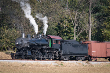 Fototapeta na wymiar A View of An Antique Steam Freight Train Approaching on a Single Track Blowing Smoke on a Sunny Day