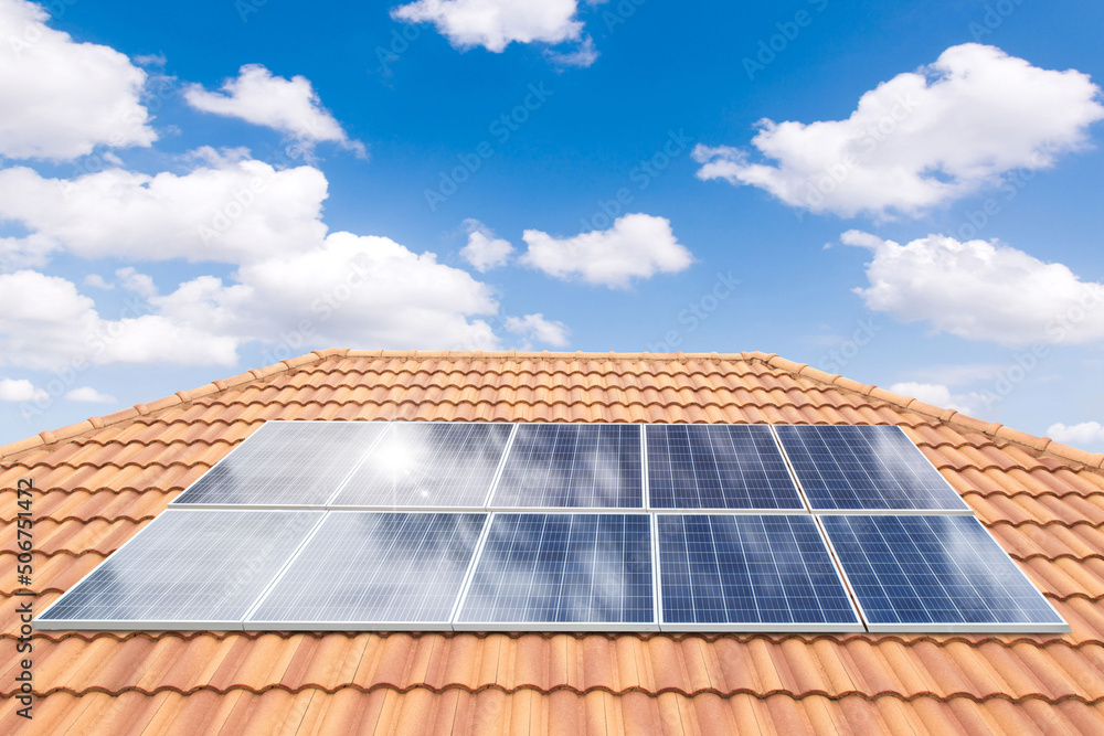 Wall mural solar panel on a red roof reflecting the sun and the cloudless blue sky