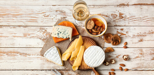 Different types of cheese with glass of wine, dried fruits and nuts on white wooden background, top...