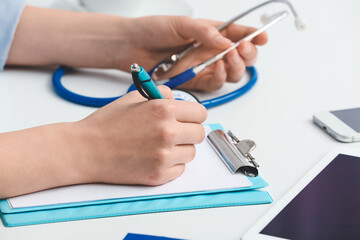 Female doctor writing in clipboard at table in clinic, closeup