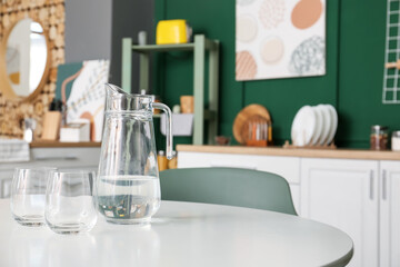 Jug with water and empty glasses on dining table in modern kitchen